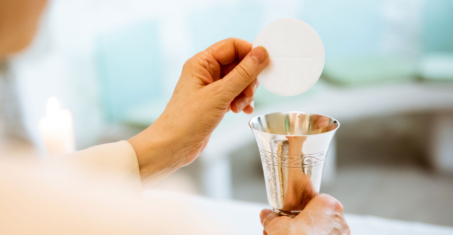 Rector holding communion wafer above silver chalice