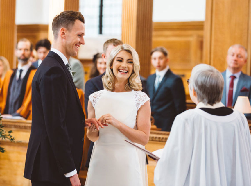 Smiling wedding couple exchanging rings in front of Rector