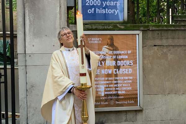 Rector Alison Joyce holding a candle in front of the closed gates of St Bride's